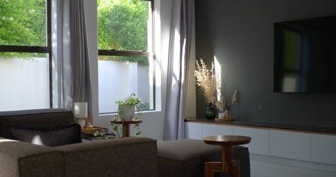 Sunlit minimalist living room with gray sectional and ottoman, greenery, textured accents