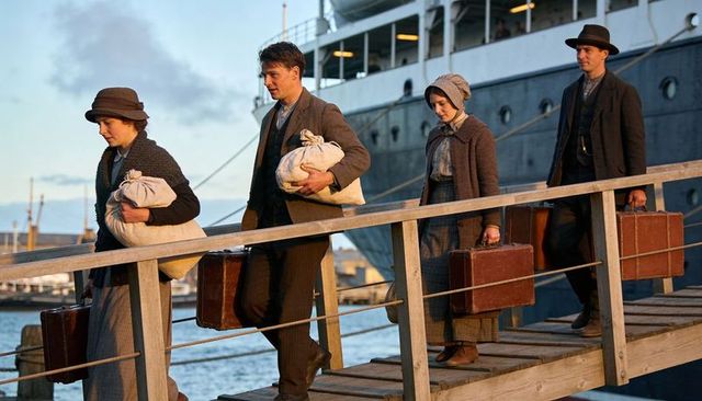 Group of passengers boarding ocean liner carrying suitcases on wooden gangplank at sunset