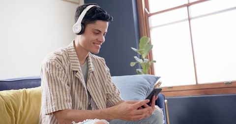 Smiling Young Man Using Smartphone with Headphones Indoors