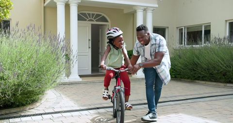 Father Teaching Daughter to Ride Bicycle Outside Home