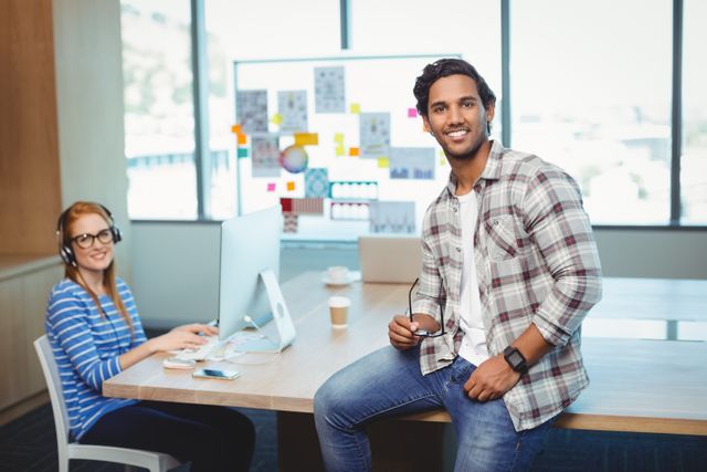 Male graphic designer sitting on desk with coworker in conference room at office