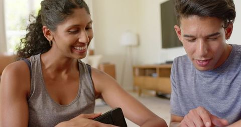 African couple sharing cozy tech moment at home smiling and pointing at smartphone and tv