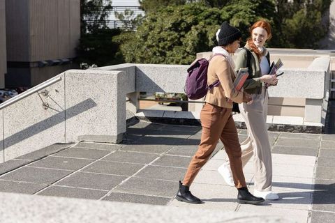 Two students walking on university campus carrying backpacks and notebooks, smiling