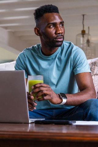Remote worker drinking green juice while using laptop on minimalist living room sofa