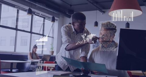 Black coworker pointing at monitor collaborating on analytics with teammate in open office