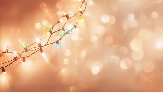 Glowing multicolor string lights casting warm bokeh on peach wall for festive ambience