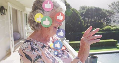 Senior woman smiling on terrace tapping virtual likes while holding mug, outdoor sunlight