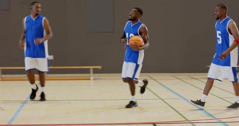 Center player dribbling down court in blue jersey 12 with teammates on indoor hardwood
