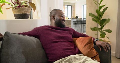 African American Man Reclining on Sofa in Cozy Open-Plan Living Space with Maroon Sweater