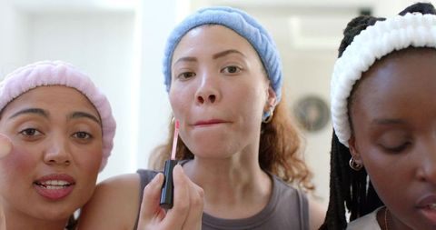 Multiracial friends applying lip gloss during morning skincare and makeup routine