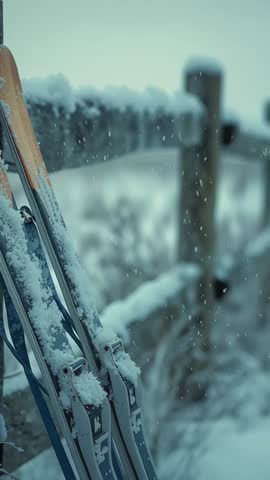 Vertical video showing snowflakes drifting on cross-country skis leaning on wooden fence