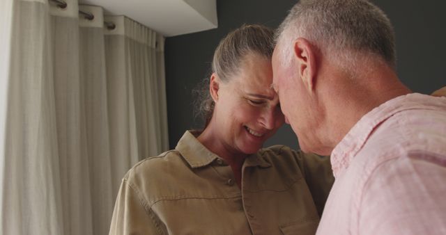 Senior couple embracing each other with love and tenderness near a window. This image depicts emotional connection and warmth between older adults, highlighting their intimate bond and mutual support. Suitable for use in content about ageing, retirement, enduring relationships, family bonds, love stories, and emotional well-being.