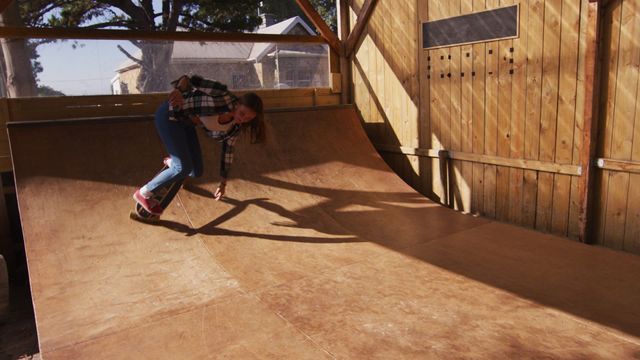 A young caucasian female skateboarder balancing on a plywood ramp in a sunlit indoor skate park. This video captures the essence of active lifestyle and enthusiasm for skateboarding as a hobby. Suitable for content related to sports, youth culture, outdoor activities, and healthy living. Can be used for skateboarding tutorials, urban lifestyle blogs, and advertisements promoting sports equipment.