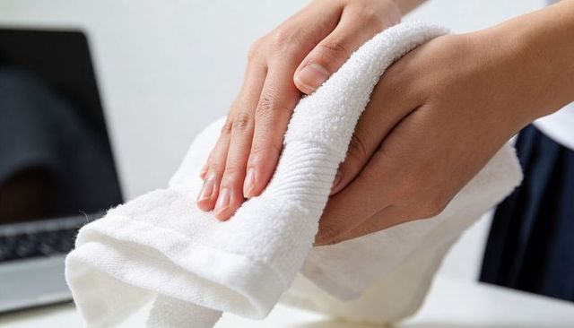 Pressing hands smoothing white terry towel on desk near laptop, home workspace linen care