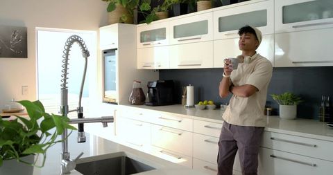 African american man leaning on modern kitchen counter holding coffee mug, morning calm