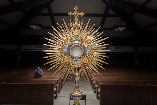 Golden Eucharistic monstrance displayed in a church. Enhancing the spiritual ambiance with its intricate design and religious significance. Useful for religious articles, church websites, sacraments, spirituality content.