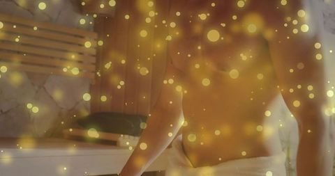 Male relaxing in sauna with golden bokeh glow, towel wrapped, wellness spa interior