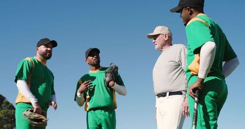 Senior coach guiding baseball team huddle on sunny field emphasizing teamwork and strategy