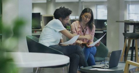 Coworkers Reviewing Documents and Collaborating in Casual Office Lounge with Laptop