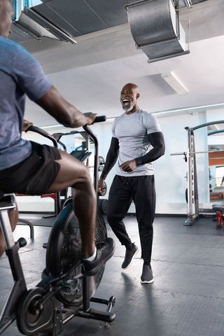 African american trainer coaching man pedaling air bike during high intensity gym session