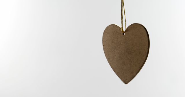 Elegant brown heart ornament hanging by a string against a light background. Perfect for valentine-themed projects, rustic decor concepts, minimalist art, and advertisement. Ideal to use in graphic design, greeting cards, social media posts, wedding invitations, and other creative projects emphasizing simplicity and elegance.