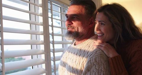 Mature Couple Enjoying Morning Sunlight Through Window Blinds, Cozy Knit Sweaters