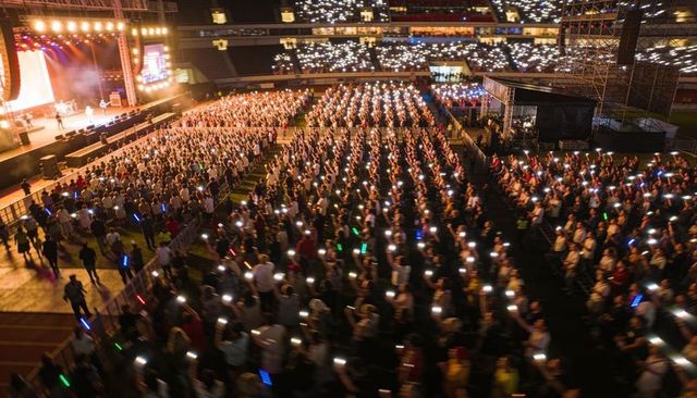 Stadium Crowd Raising Smartphones and Glow Sticks During Night Concert Under Stage Lights