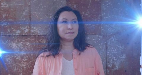 Woman Gazing Right Wearing Peach Shirt Against Rusted Metal Wall with Blue Light Flares