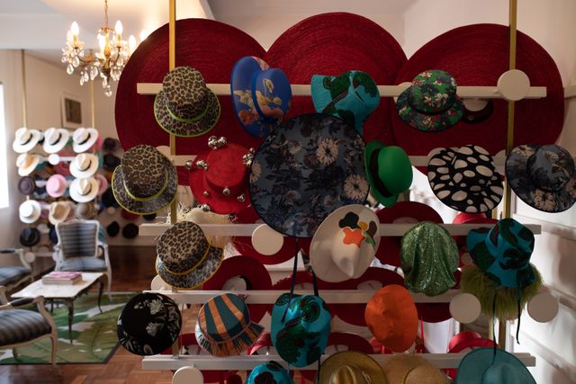 Front view of various styles of hats for women displayed in rows on the white walls of the showroom at a hat makers. 
