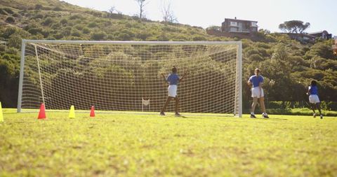Children Practicing Soccer with Goal and Cones on Sunlit Field