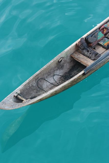Close up of a traditional wooden canoe floating on calm turquoise water, emphasizing the simplicity and craftsmanship of the boat. This can be used in content about traditional boating techniques, travel destinations, or ocean-themed materials. Ideal for travel blogs, brochures, or advertisements focusing on coastal and maritime experiences.