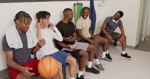 Diverse male basketball teammates laughing and passing earbuds while leaving locker room