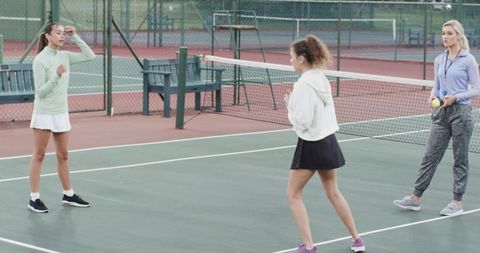 Female tennis players practicing drill with coach on outdoor hardcourt near net
