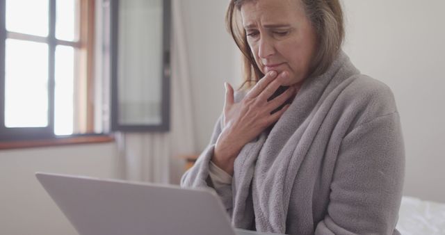 Mature woman expressing concern while using a laptop in a cozy room, possibly encountering a problem. Great for illustrating themes of senior technology use, problem-solving, online security, or medical consultations.