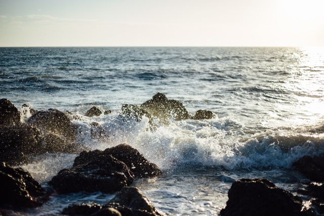 Rough waves crashing against coastal rocks with sun reflecting off the water. This captivating scene conveys nature's power and beauty, perfect for travel reviews, environmental campaigns, or backgrounds for websites promoting outdoor activities.