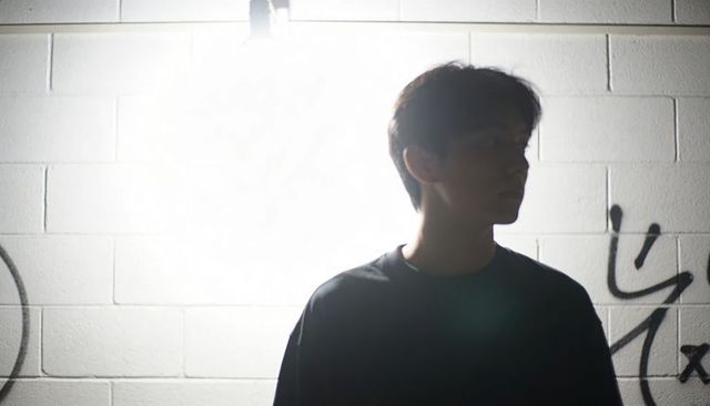 Backlit teen silhouette against graffiti cinderblock wall under bright alley lamp