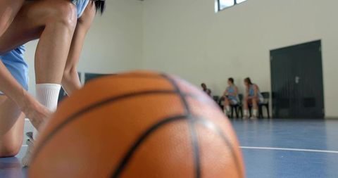 Basketball on indoor court with kneeling player tying shoe and bench teammates