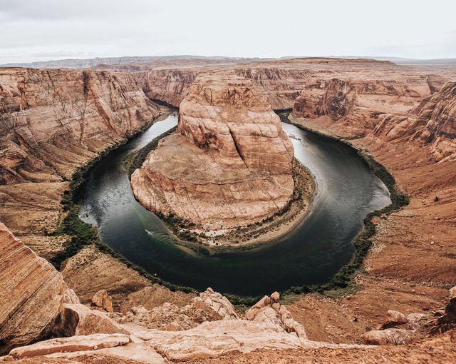 This visual depicts an aerial perspective of the Horseshoe Bend around the Colorado River, nestled in Arizona's unique geological landscape. Perfect for travel guides, nature blogs, educational materials on geological formations, promotional tourism posters, and scenic desktop backgrounds.