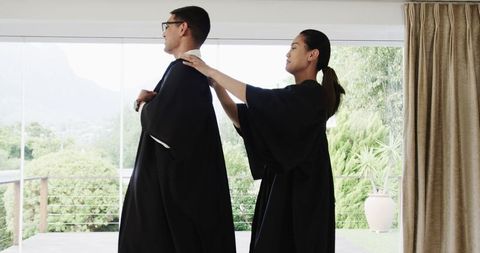 Graduating couple adjusting gowns with joyful expression