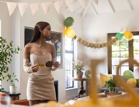Young woman standing in decorated living room holding gold medallion at birthday celebration