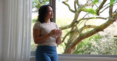 Mid adult woman relaxing with mug by window in natural light