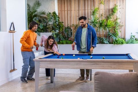 Diverse friends playing pool and socializing in lounge with blue felt table and plants