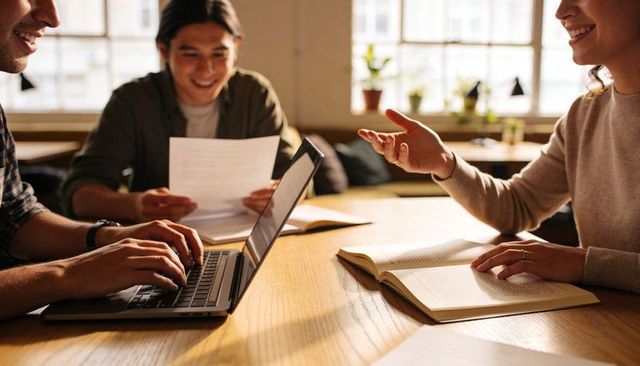 Three Colleagues Collaborating Around Laptop and Documents on Sunlit Wooden Table