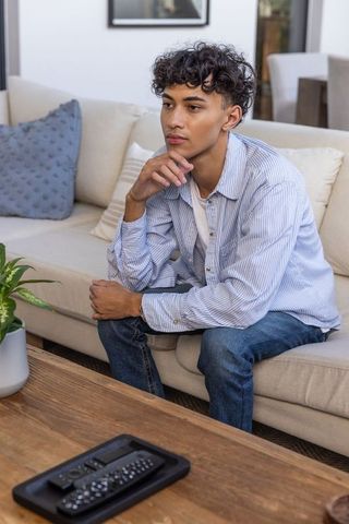 Young Man Relaxing on Sofa with Remote Controls in Modern Living Room