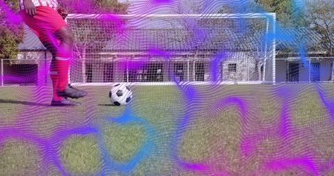 Goal-line shot taking mid-adult soccer player wearing red shorts with purple overlay