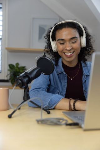 Nonbinary podcaster recording in cozy home studio with headphones, microphone, laptop