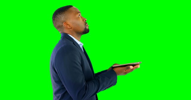 African American businessman holding tablet ready for work scenarios. Green screen background allows for easy customization; good for use in business presentations, tech reviews, or marketing materials.