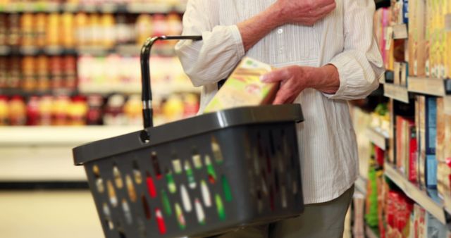 Senior customer holding shopping basket while choosing groceries in a supermarket aisle. Ideal for themes of elderly lifestyle, shopping, market research, consumer behavior, grocery shopping needs for seniors, retail advertising, and health-conscious choices.