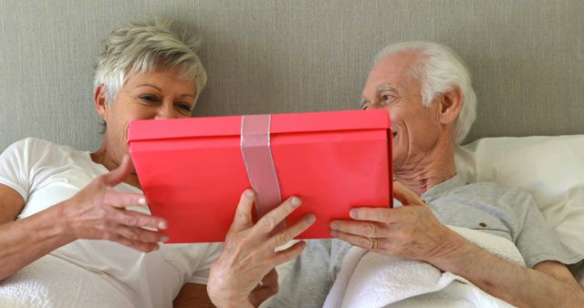 Senior man giving a surprise gift to woman in the bedroom at home