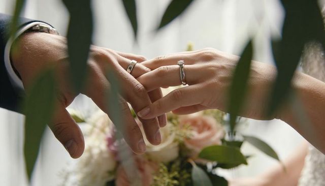 Exchanging wedding rings through foliage with pastel bouquet and soft window light